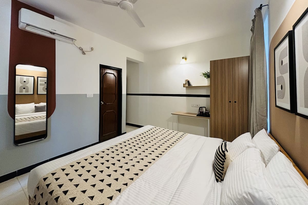 A hotel room with a bed, a desk, a wardrobe, a ceiling fan, and a mirror.