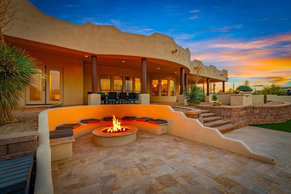 A modern outdoor patio with a fire pit, seating area, and a view of the sunset.
