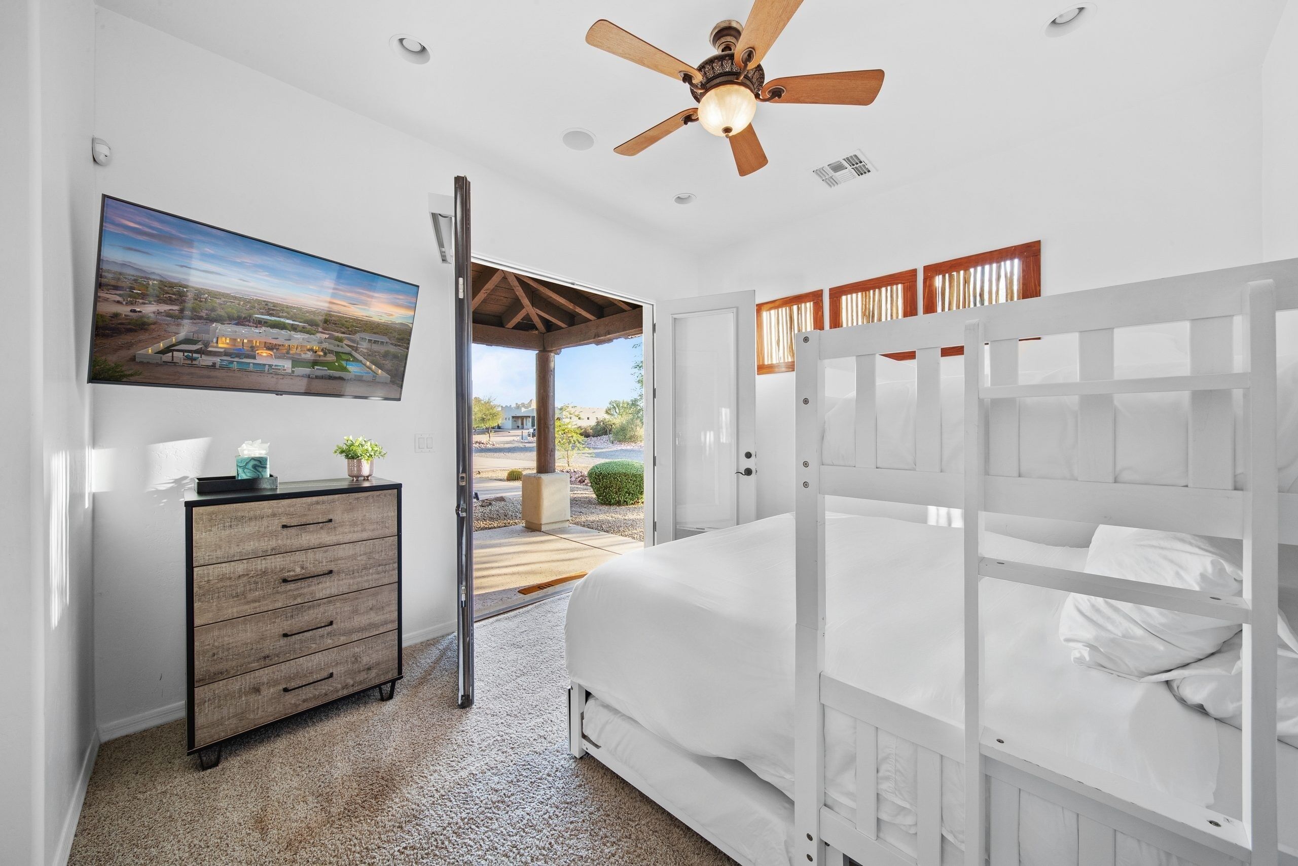 A bedroom with a bed, a dresser, a ceiling fan, and a view of the outside.