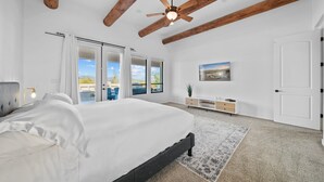 A bedroom with a bed, a ceiling fan, a large window with curtains, a view of the outdoors, and a door. - Casa Verde 4 Bedroom Home by RedAwning (Scottsdale)