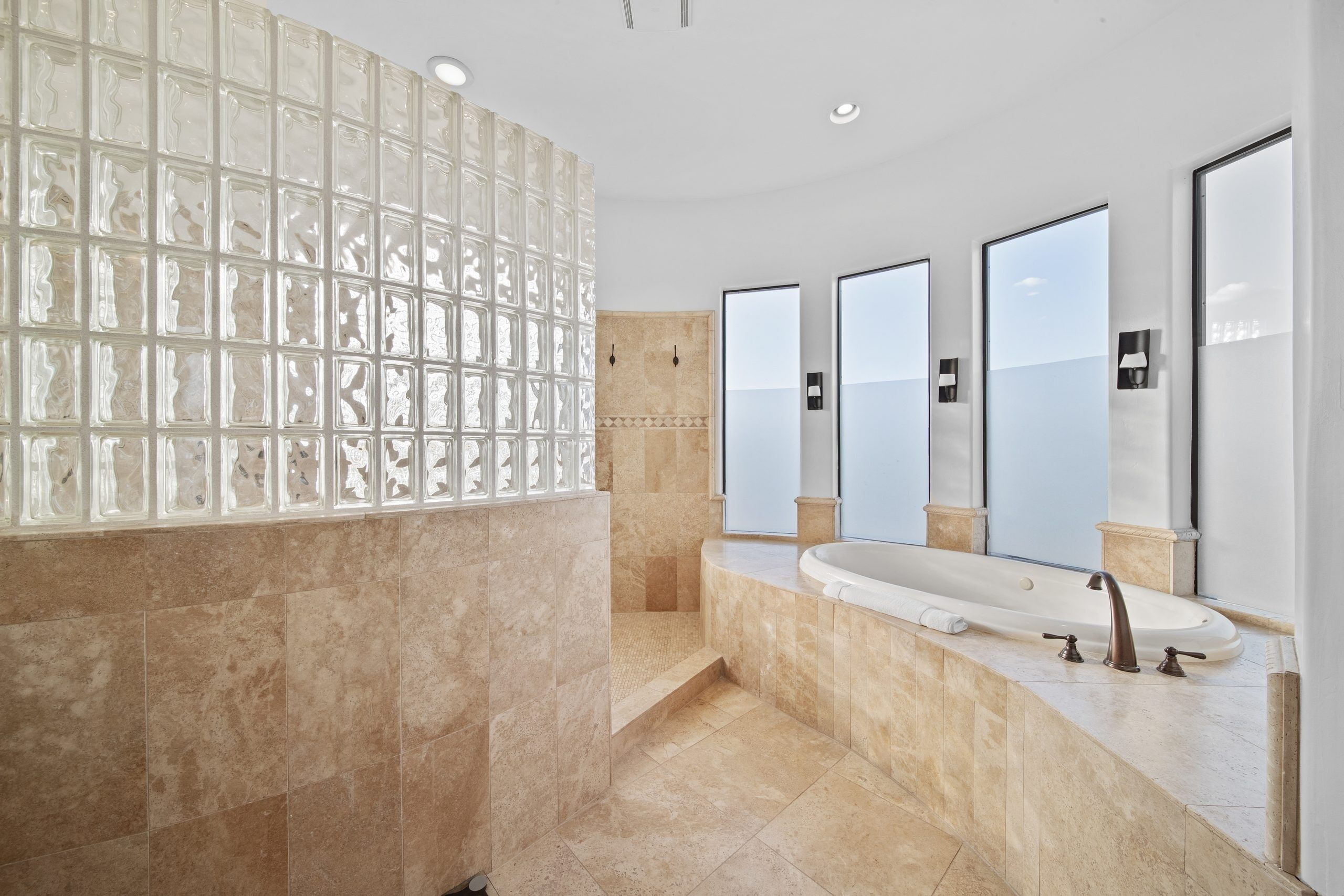 A modern bathroom with a large glass block wall, a freestanding bathtub, and three wall-mounted mirrors.