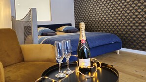 Une chambre moderne avec un lit, un canapé, une petite table sur laquelle se trouvent une bouteille de champagne et des verres, et un mur orné d’un motif.