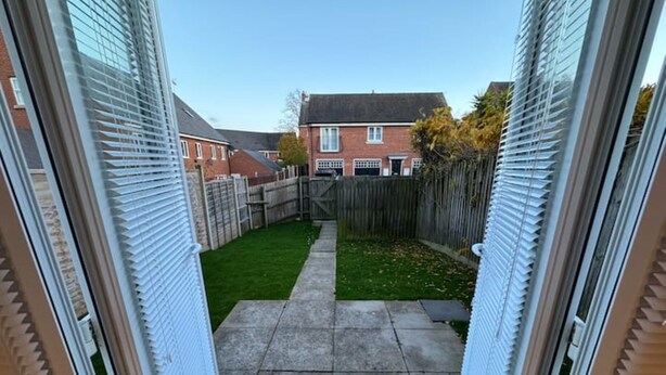 Un sendero estrecho que conduce a un patio trasero pequeño con césped y una valla de madera.