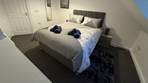 Un dormitorio con cama, mesita de noche, lámpara de pared y una puerta.