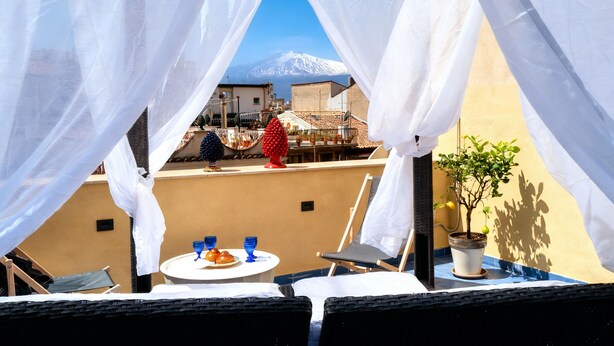 A terrace with a table and chairs, a potted plant, and a view of a mountain. - Live the Magic of Taormina Where History, Beauty, and Sicilian Soul Meet (Taormina)