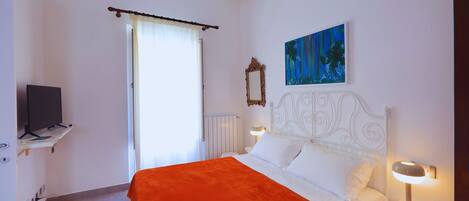 A hotel room with a bed, a television on a shelf, a painting on the wall, and a window with curtains.