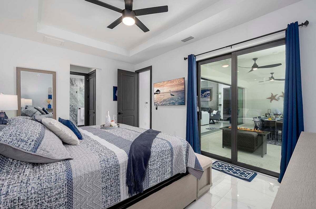 Ein modernes Schlafzimmer mit einem großen Bett, einem Deckenventilator und einer Schiebeglastür, die in einen Wohnbereich führt.