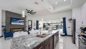 A modern kitchen with a marble countertop, stainless steel appliances, and a view to an outdoor pool area.