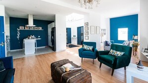 Un vaste espace de vie agrémenté d’un mur d’accent bleu, d’un fauteuil vert, d’une table basse en bois et d’un lustre.