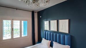 Une chambre à coucher avec un lit, un lustre et trois œuvres d’art encadrées accrochées au mur.