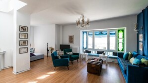 Un salon spacieux avec une grande fenêtre, un lustre et un canapé bleu.