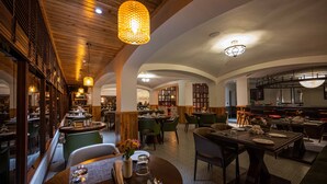 A restaurant with wooden ceiling beams, round tables, and green chairs. - Udaan Hotel Pine Crest (Gyalshing)