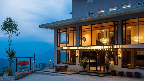 A hotel with a large entrance, outdoor seating, and a view of the mountains. - Udaan Hotel Pine Crest (Gyalshing)