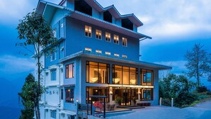 A two-story hotel with large windows and a balcony, surrounded by trees. - Udaan Hotel Pine Crest (Gyalshing)