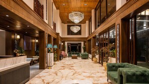 A spacious lobby with a marble floor, a chandelier, and green upholstered sofas. - Udaan Hotel Pine Crest (Gyalshing)
