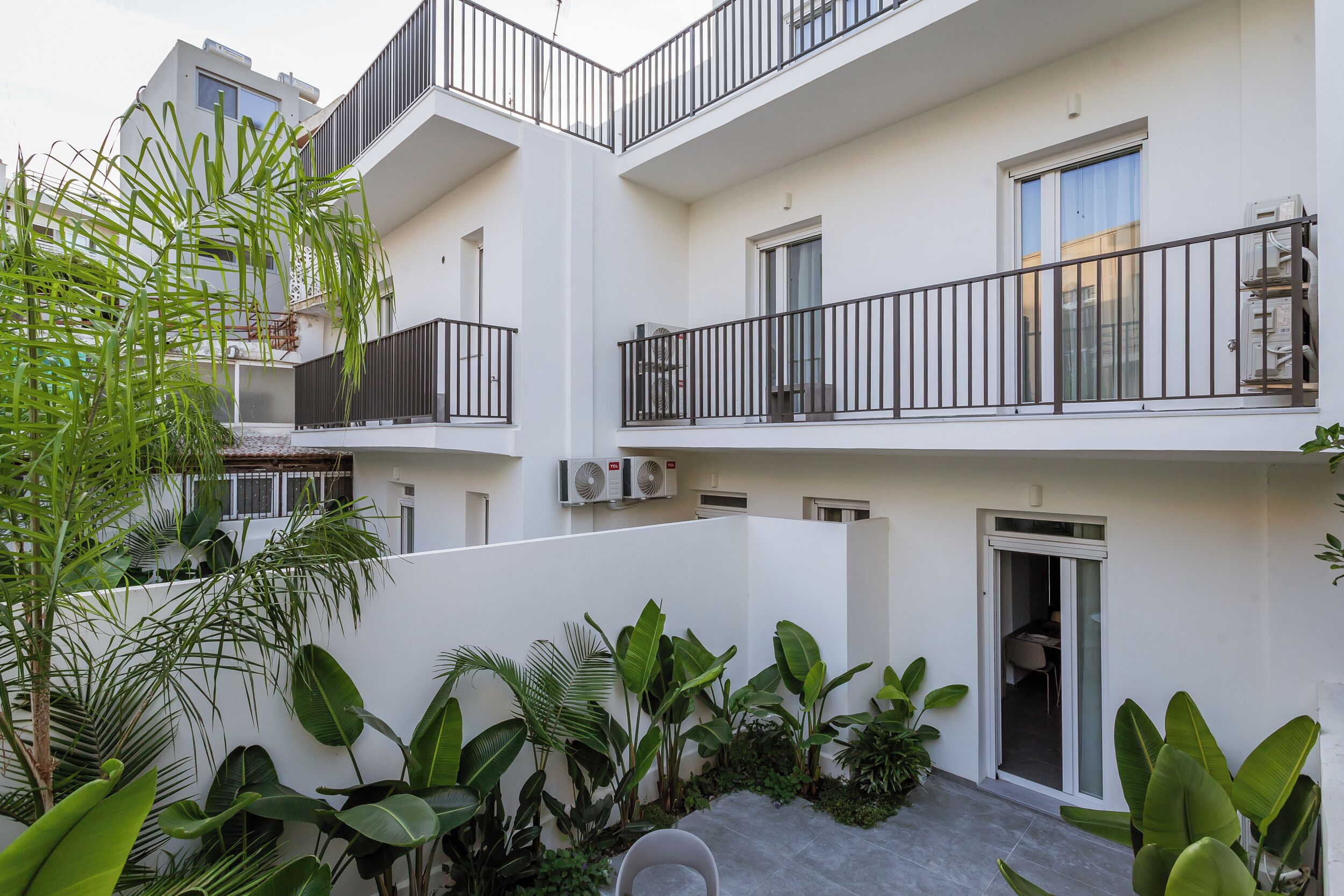 Un edificio residencial de varios pisos con balcones, unidades de aire acondicionado y abundante vegetación.