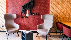 A modern interior with two grey armchairs, a wooden table, and a red textured wall with a black abstract sculpture. - DAS PALMBERGER (Spiegelau)