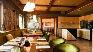 A restaurant with wooden walls and green upholstered chairs. Tables are set with menus and cutlery. - DAS PALMBERGER (Spiegelau)