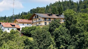 A multi-story building with balconies, surrounded by dense forest. - DAS PALMBERGER (Spiegelau)