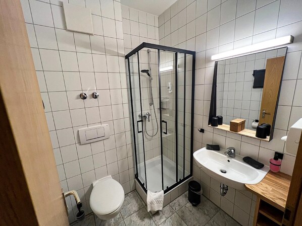 Ett modernt badrum med en dusch som är avskärmad med glasväggar, en vit toalett och ett handfat med en spegel ovanför.
