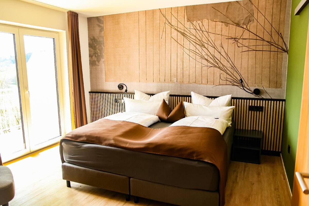 A modern bedroom with a large bed, a headboard with vertical lines, a bedside table, and a view of the outdoors through a sliding door.