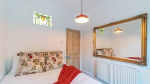 A bedroom with a bed, floral pillows, a red blanket, a large mirror, a hanging light, and a stained glass window. - Family Stay | By Sefton Park & Lark Lane | Parking (Liverpool)