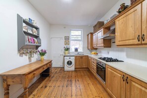 A compact kitchen with wooden cabinets, a washing machine, and a stove. - Family Stay | By Sefton Park & Lark Lane | Parking (Liverpool)