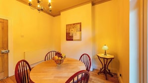 A dining room with a wooden table, four chairs, a fruit bowl, a chandelier, a painting, and a table lamp. - Family Stay | By Sefton Park & Lark Lane | Parking (Liverpool)