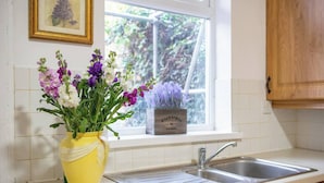 A kitchen with a yellow vase of flowers on the counter, a window with a view of greenery, and a wooden cabinet. - Family Stay | By Sefton Park & Lark Lane | Parking (Liverpool)