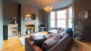 A cozy living room with a fireplace, a sofa, a television, and a chandelier. - Family Stay | By Sefton Park & Lark Lane | Parking (Liverpool)