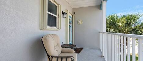 A covered porch with a beige chair, a small table, and a wall-mounted clock.