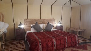 Una habitación con cabecera de madera, cama con manta roja, dos mesitas de noche con faroles y una alfombra estampada.