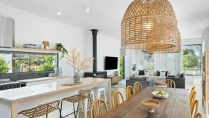 A modern kitchen with a central island, dining area with wooden table and chairs, and a large woven light fixture.