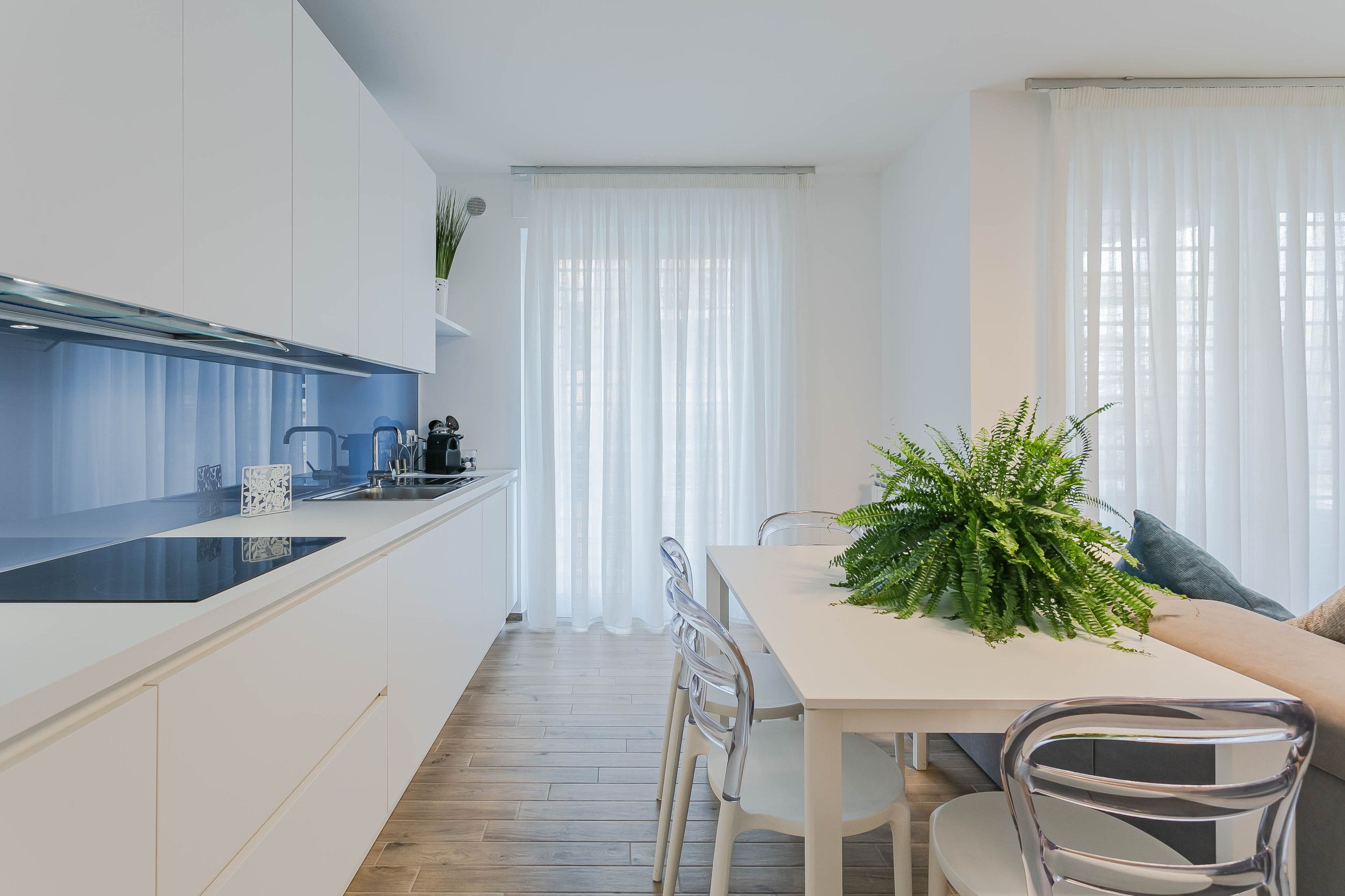 Una cocina moderna con encimera blanca, electrodomésticos de acero inoxidable y un comedor con mesa y sillas blancas.