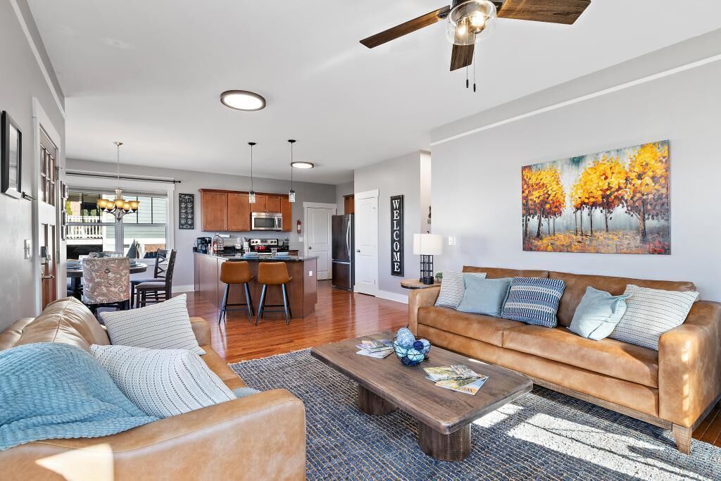 A spacious living room with a leather sofa, a coffee table, and a painting of autumn trees.