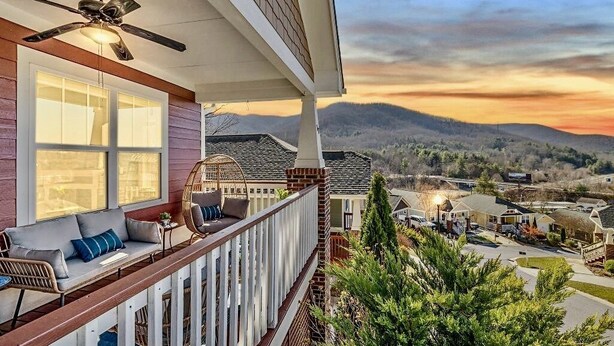 A balcony with a ceiling fan, a sofa with cushions, and a view of a residential area with houses and mountains in the background. - Mountain Views, Game Room, Hot Tub –Close to Downtown (Asheville)