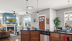 A modern kitchen with wooden cabinets, a central island, and a dining area with a fireplace. - Mountain Views, Game Room, Hot Tub –Close to Downtown (Asheville)