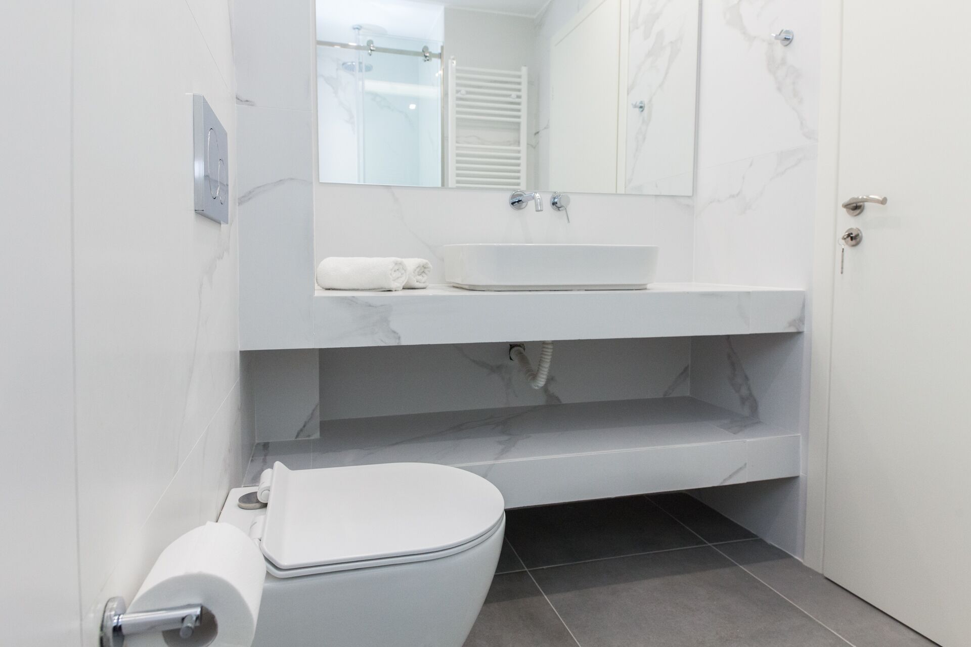 Une salle de bain moderne avec des toilettes blanches, un meuble-lavabo avec un miroir et un espace douche.