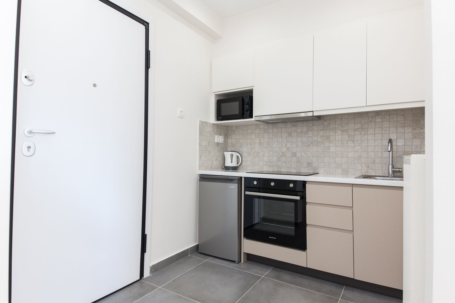 A compact kitchen with white cabinets, a microwave, a kettle, a dishwasher, and an oven.