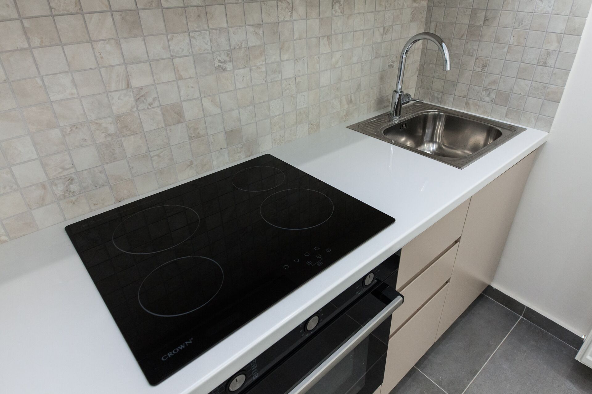 A kitchen with a black induction cooktop, a stainless steel sink, and a white countertop.