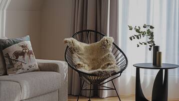 Una sala moderna con un sofá gris, una silla de estructura metálica negra con una manta de piel, una mesita redonda con una planta y cortinas traslúcidas.