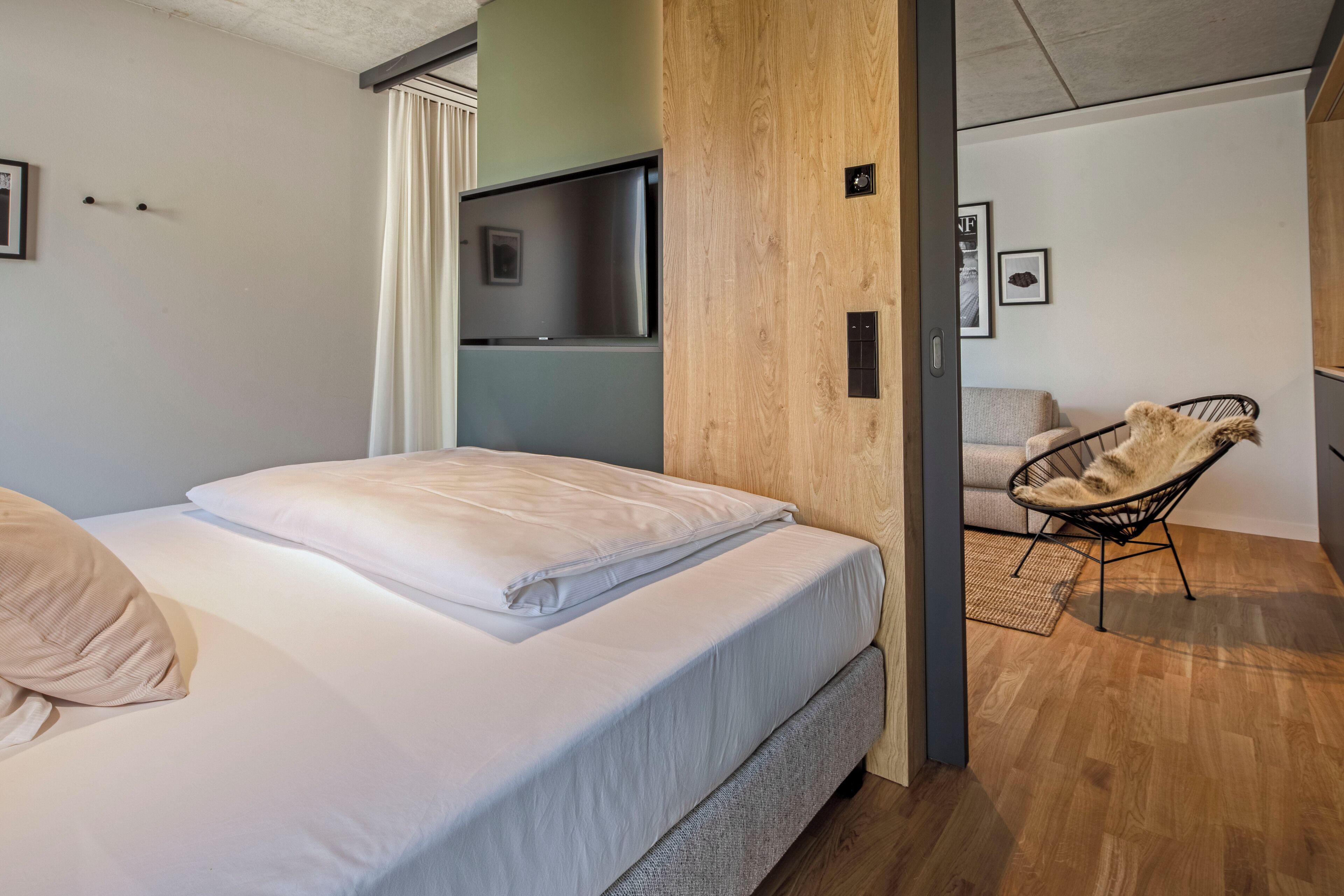 A modern bedroom with a bed, a wooden wall, a TV, and a chair.