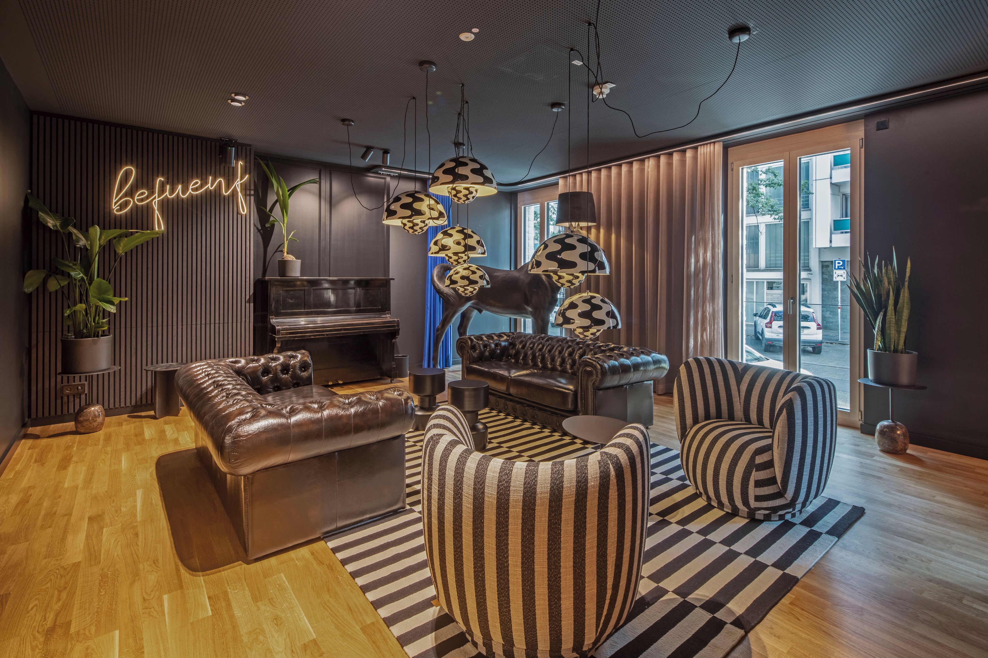 A modern living room with leather sofas, striped armchairs, and a neon sign.