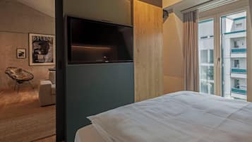 Ein modernes Hotelzimmer mit einem großen Bett, einem Flachbildfernseher, einem Holzschrank, einer kleinen Sitzecke und Blick auf die Stadt.