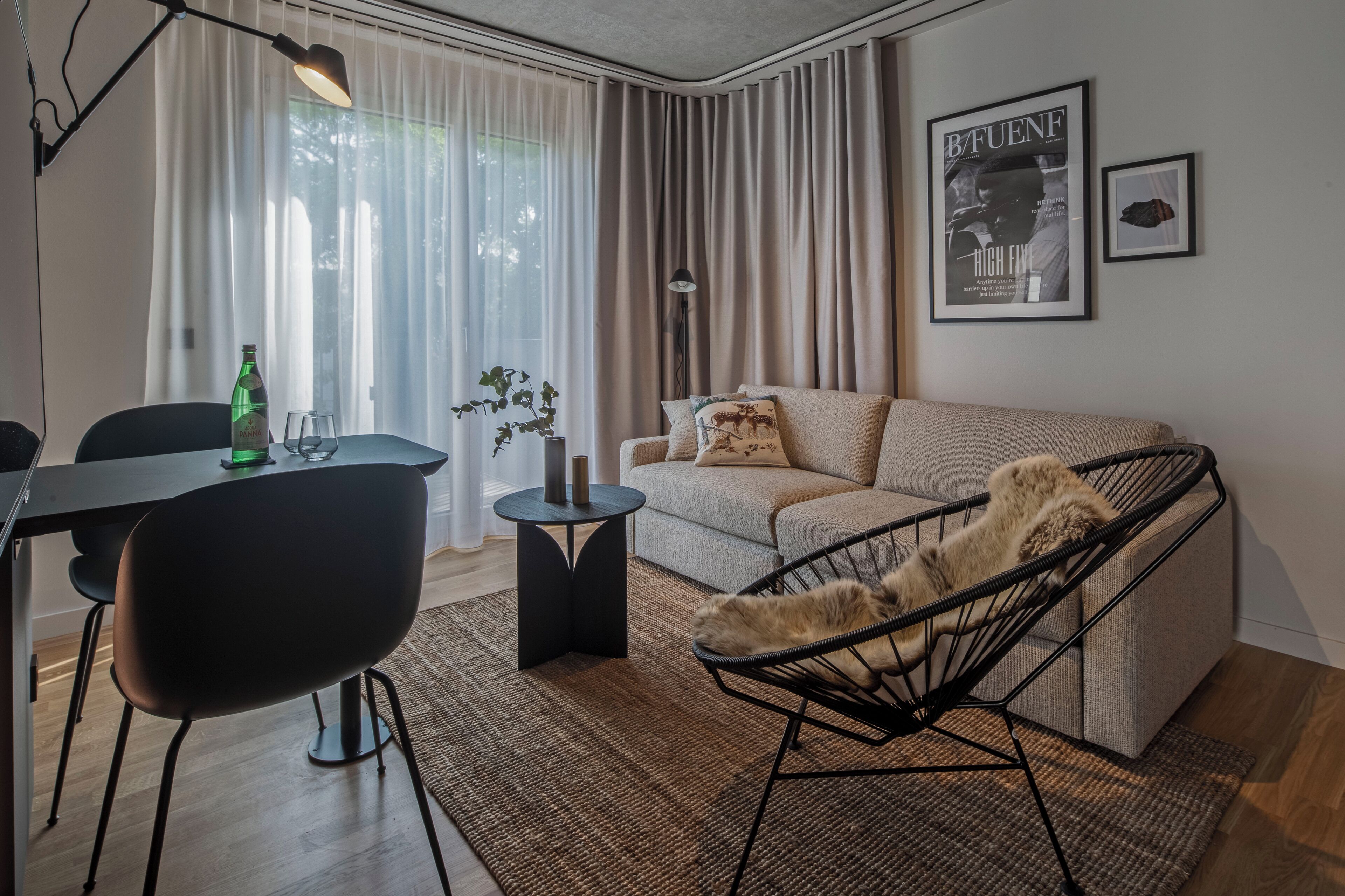 Ein modernes Wohnzimmer mit einer Couch, einem Esstisch mit Stühlen, einem kleinen Beistelltisch und einem schwarzen Sessel.