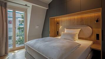 A modern bedroom with a large bed, a wooden headboard, and a view of a balcony.