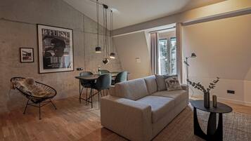 A modern living room with a sofa, a chair, a dining table, and a poster on the wall.