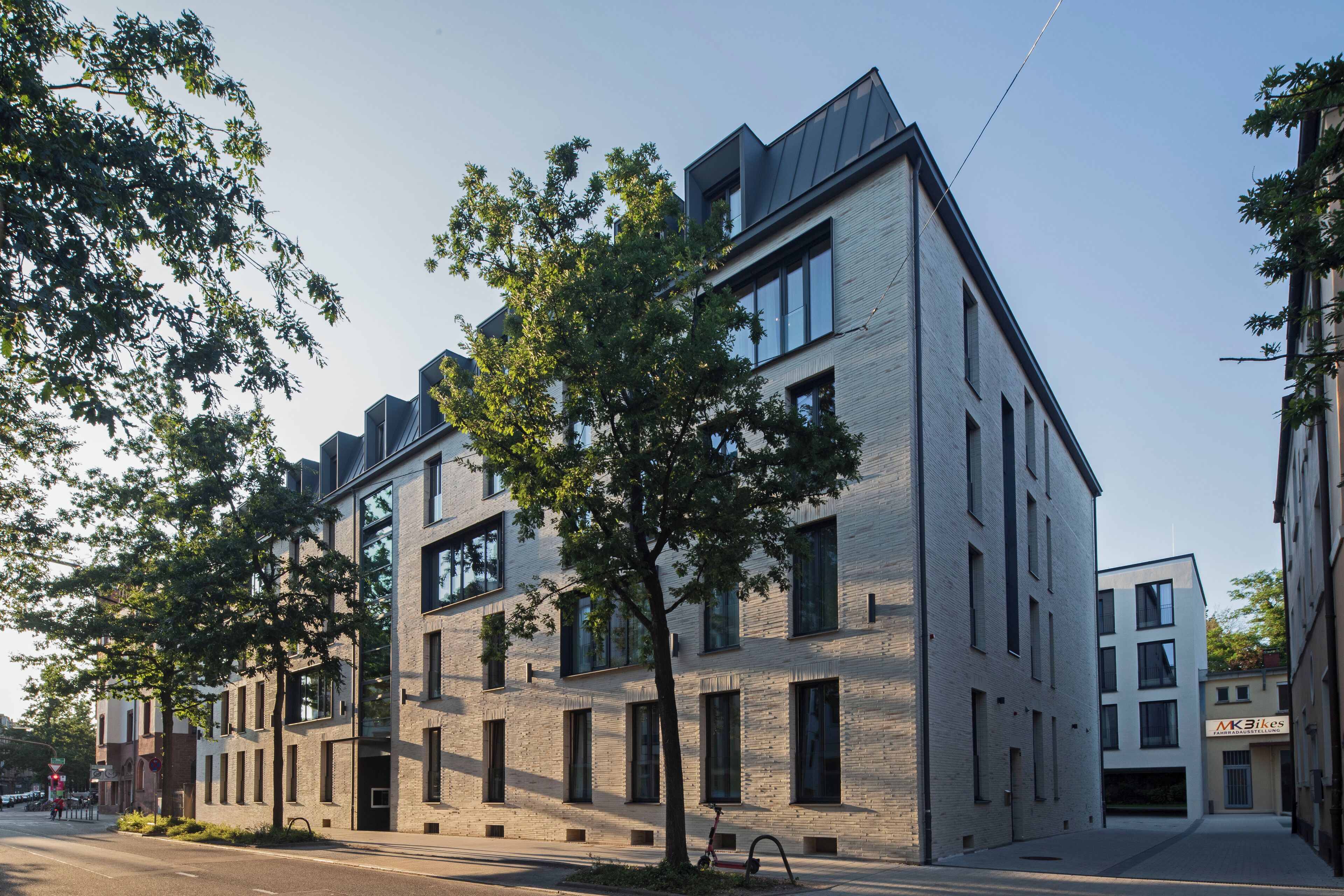 Un bâtiment moderne avec une façade en briques, de grandes fenêtres et un arbre devant.