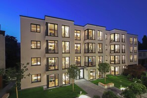 A modern multi-story building with illuminated windows and balconies, a well-maintained lawn, and a paved walkway. - B5 Apartments (Karlsruhe)
