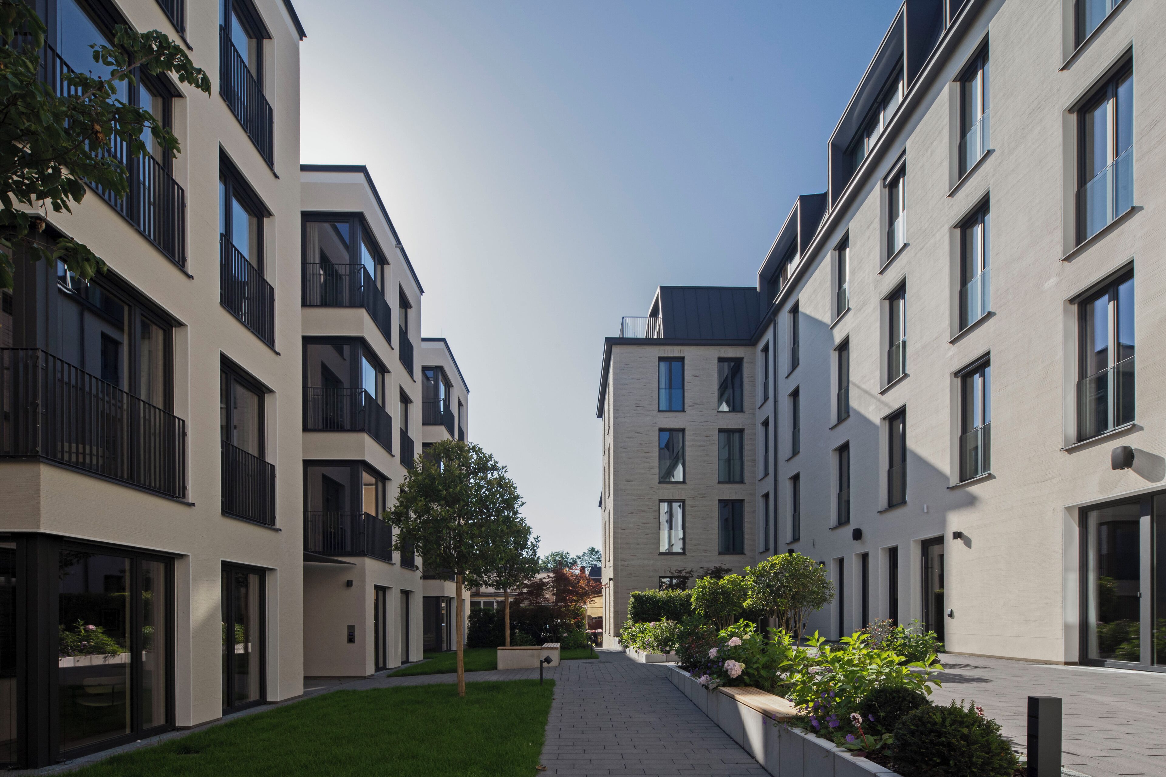 Ein moderner Wohnkomplex mit Innenhof, Balkone, großen Fenstern und einem gepflegten Rasen.